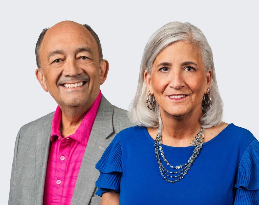 At left, a smiling older man in a grey jacket and a pink shirt. At right is an older woman with shoulder length grey hair in a turquoise top and wearing a beaded necklace.