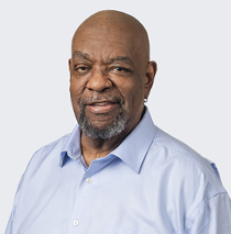An older, bald African American man in a lavender oxford shirt smiles.